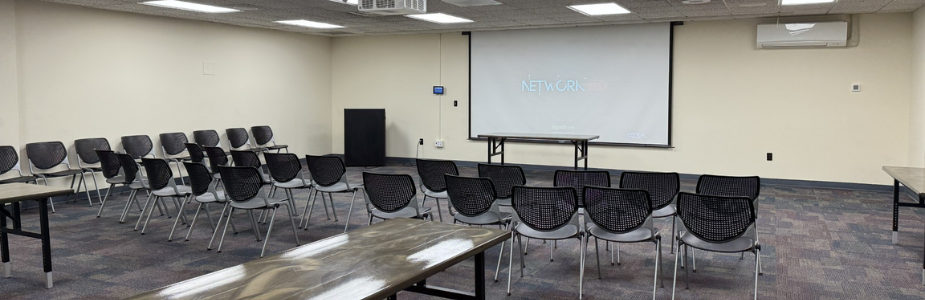 Room with presentation screen on wall and chairs facing screen.